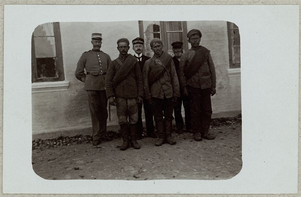Tre russiske krigsfanger med vagter foran hus